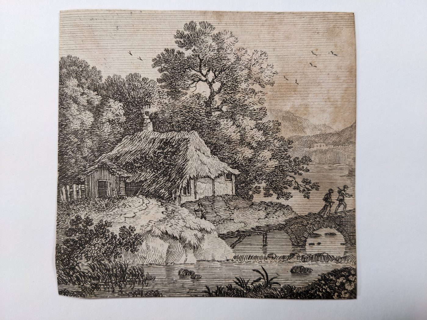 Two people crossing a bridge near a hut